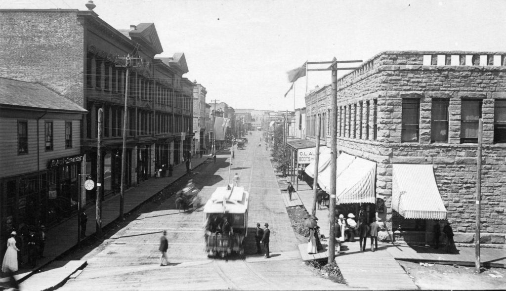 View of West Cordova from Carrall Street, showing brick buildings on either side of street with tramcar on road.